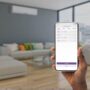 A smartphone screen showing a smart home app controlling lights and thermostat in a cozy living room.