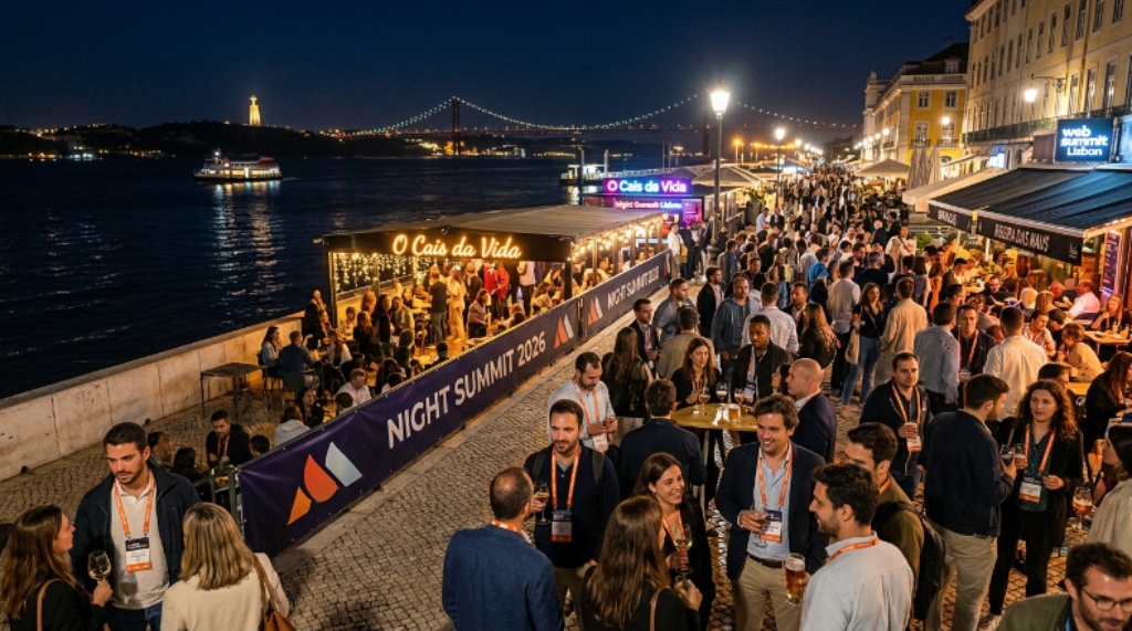Nighttime view of Lisbon's Cais do Sodré district during Night Summit 2026, with attendees socializing outside a waterfront bar along the Tagus River